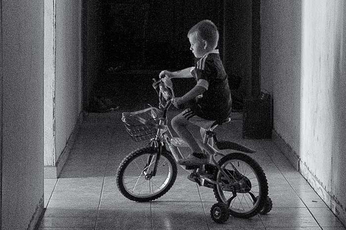 Arman Buljić na biciklu u mračnom hodniku izvan svoje trošne kuće | Arman Buljic and his bicycle in the dark hallway outside his barrack apartment.